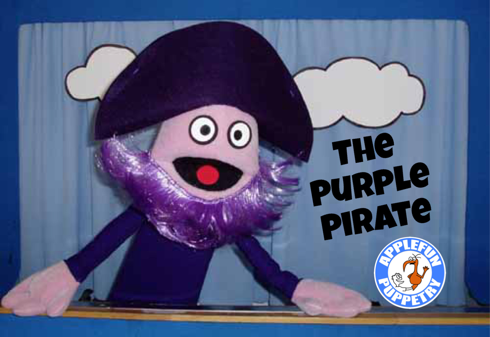 An image with a blue curtain backdrop with clouds, and a purple pirate puppet smiling