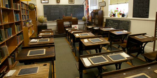 Rows of old fashioned school desks in front of a blackboard. 